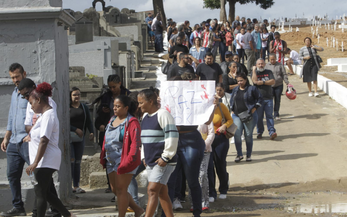 &Eacute;rica Oliveira, esposa de David, e outros familiares seguraram cartaz com pedido de paz nas comunidades durante o sepultamento