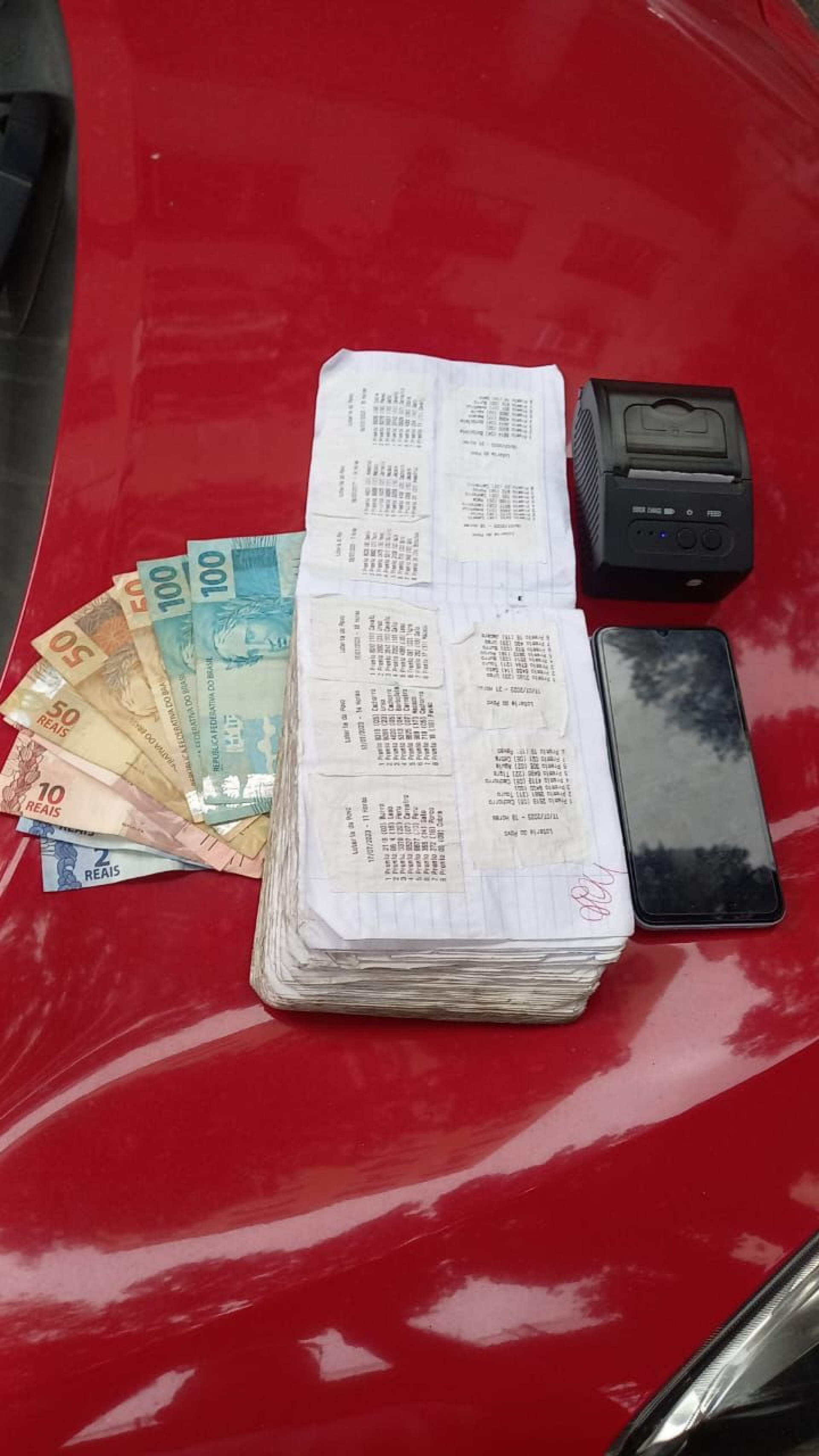 Impressora sem marca, celular, caderno com anotações do jogo do bicho e dinheiro apreendidos