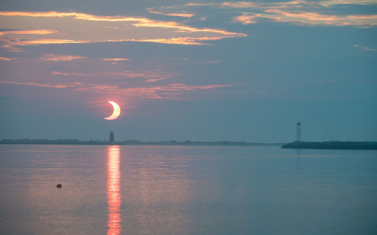 A partial solar eclipse is seen as the sun rises behind the Delaware Breakwater Lighthouse, Thursday, June 10, 2021, at Lewes Beach in Delaware. The annular or ?ring of fire? solar eclipse is only visible to some parts of Greenland, Northern Russia, and Canada. Photo Credit: (NASA/Aubrey Gemignani)