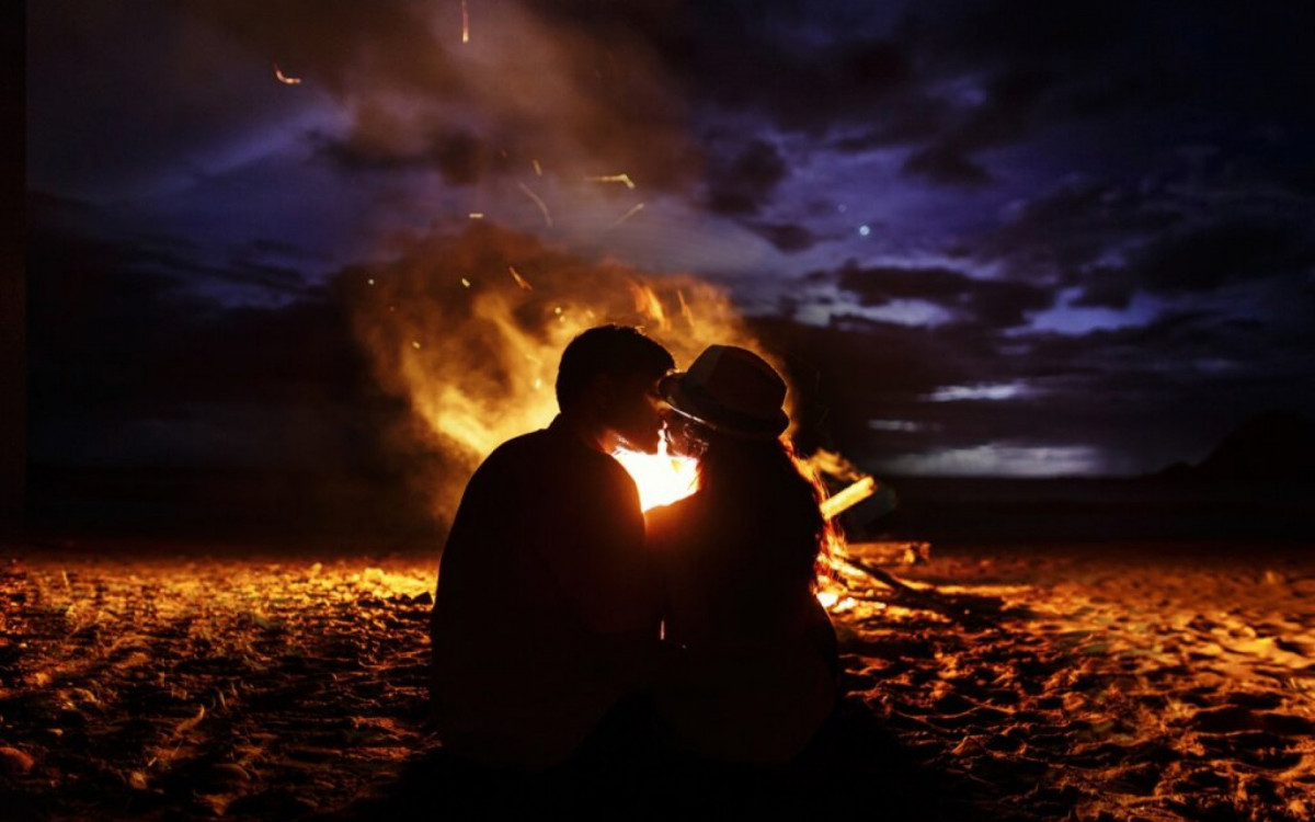 Kissing couple sits before a fireplace on the beach