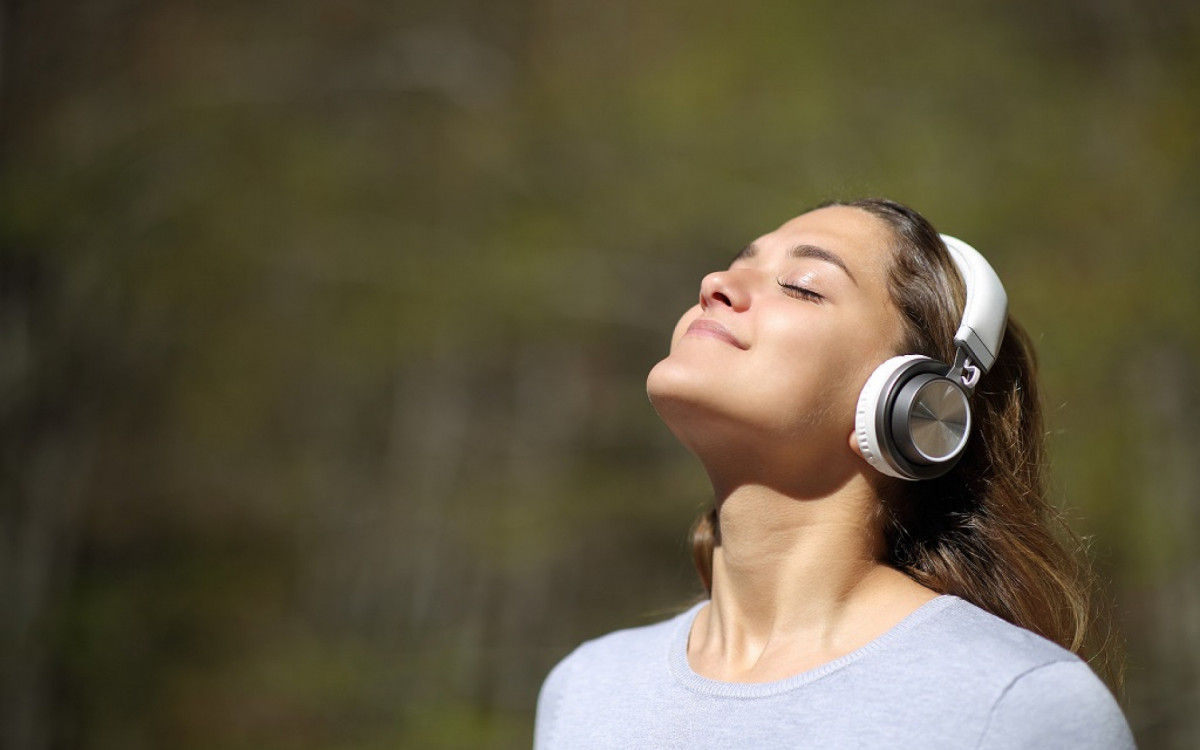Happy woman meditating wearing wireless headphones in a park