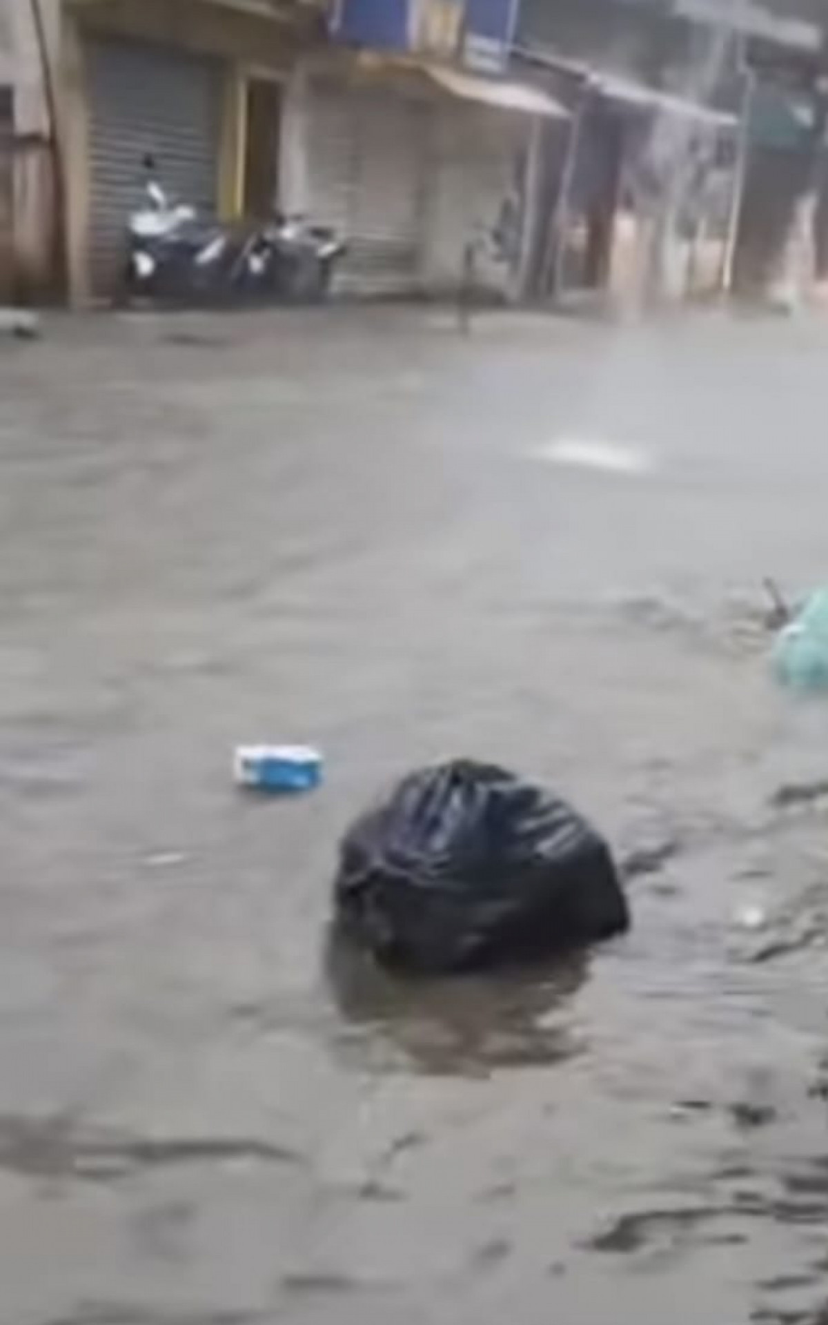 Sacos de lixo boiam na rua principal do Encruzo da Enseada inundada com o temporal desta manhã