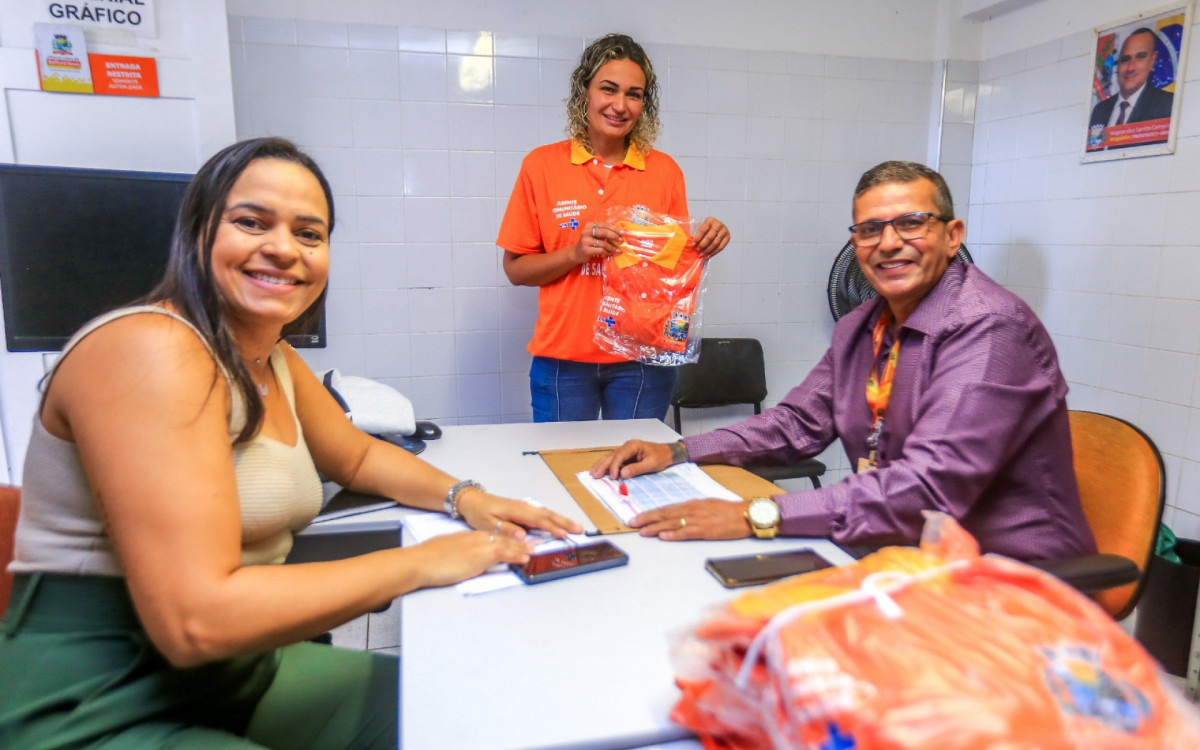 A agente Mercês (centro) recebe o novo uniforme do coordenador dos Agentes Comunitários de Saúde, Admilson Figueiredo (dir)