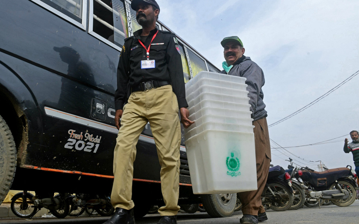 Fiscais carregam caixas usadas para coletar os votos durante as eleições no Paquistão nesta quarta-feira (7)