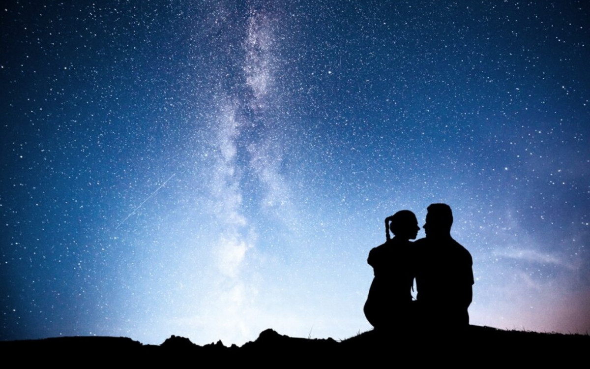 Milky Way with silhouette of people. Landscape with night starry sky. Standing man and woman on the mountain with star light. Hugging couple against purple milky way. Beautiful galaxy. Universe.