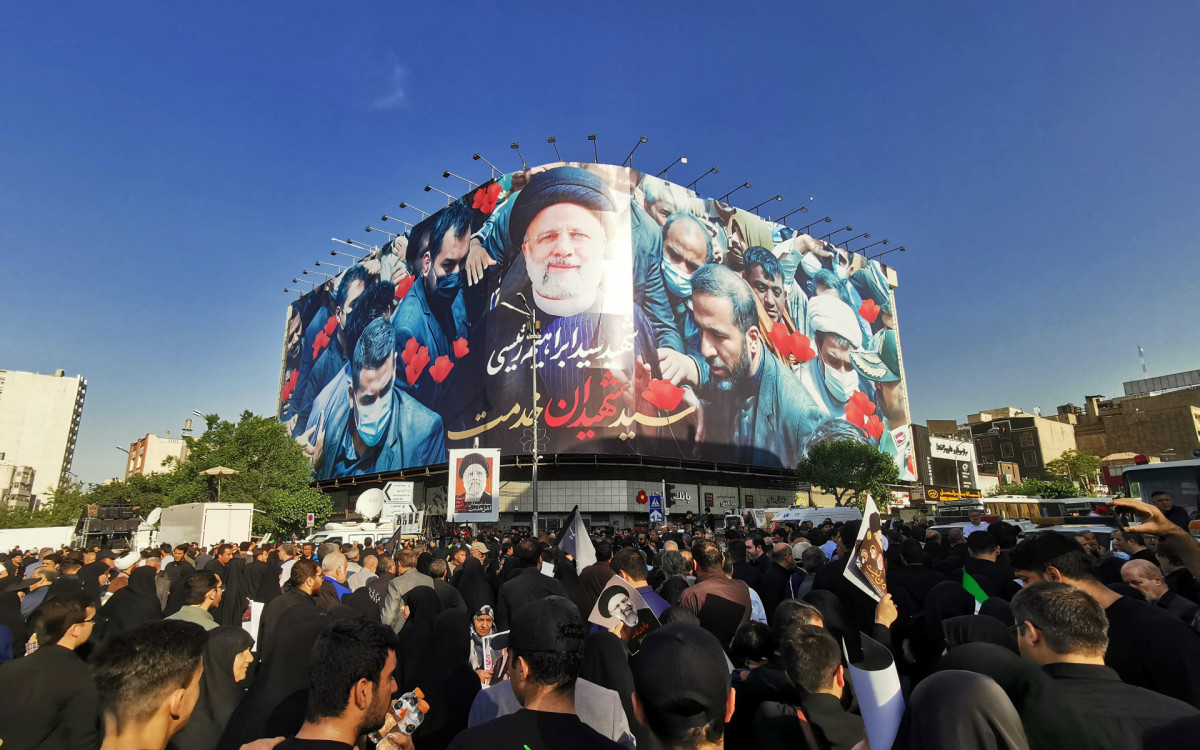 Pessoas em luto seguram cartazes do presidente iraniano, Ebrahim Raisi - AFP