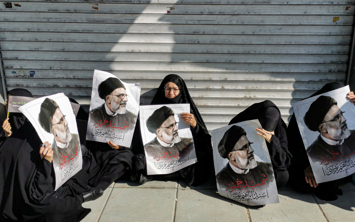 Pessoas em luto seguram cartazes do presidente iraniano, Ebrahim Raisi
