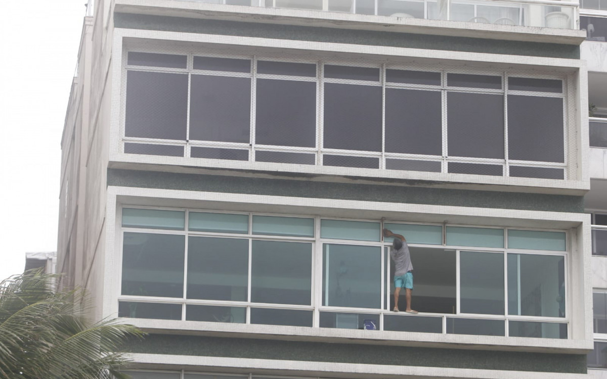 Homem limpa janela no quarto andar de prédio sem qualquer equipamento de segurança