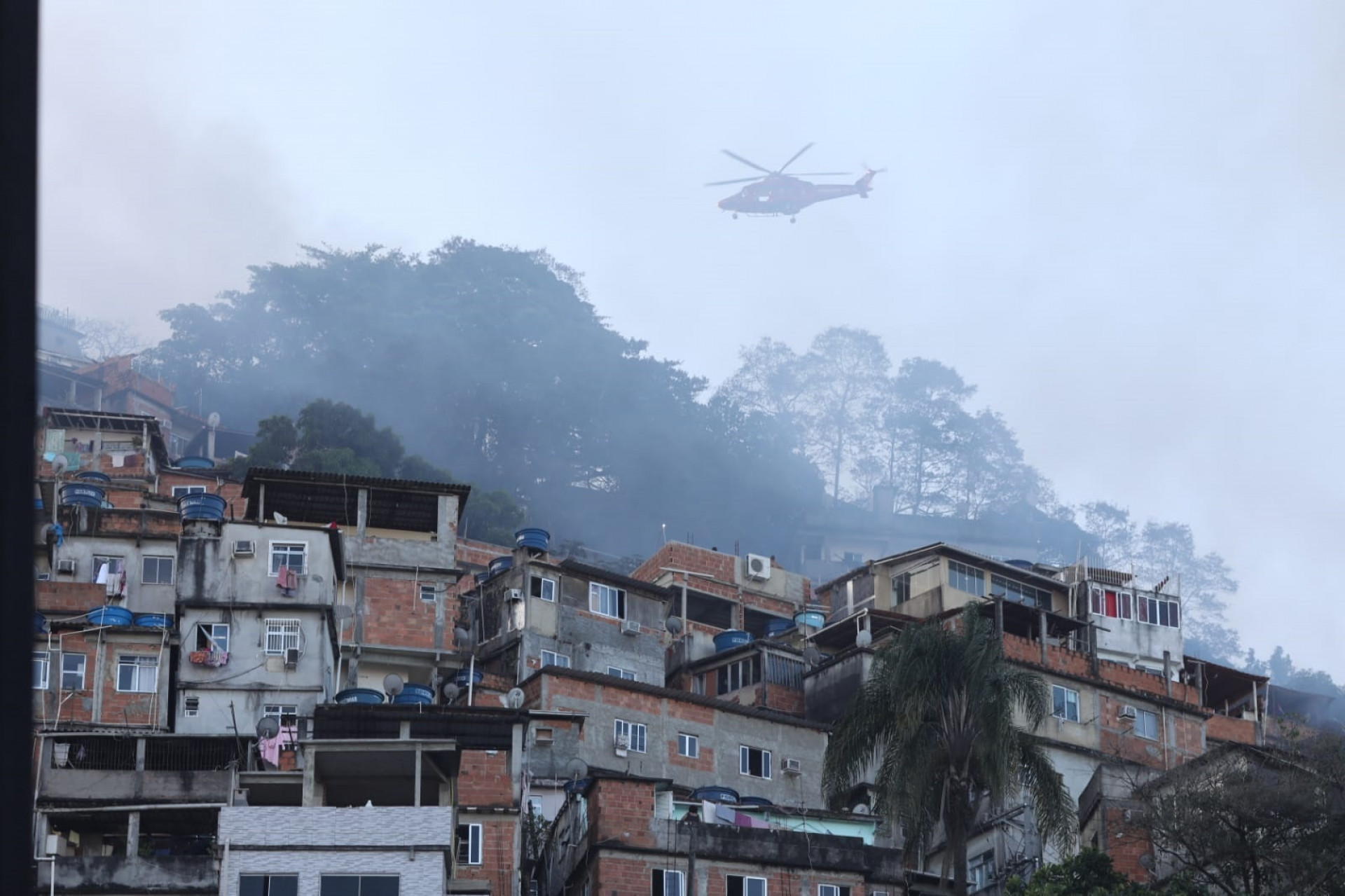 Bombeiros a bordo de um helicóptero tentam conter o fogo próximo às residências da comunidade - Pedro Teixeira/ Agência O Dia