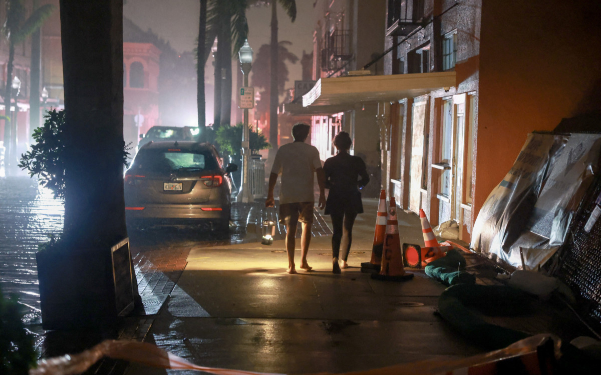 Pessoas caminham na calçada ao lado de uma rua alagada em Fort Myers