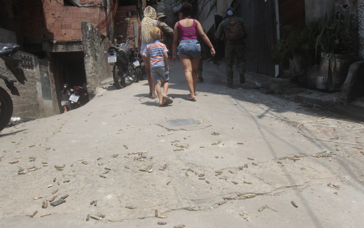 Moradores andam por cima de cápsulas deflagradas e ao lado de policiais durante operação