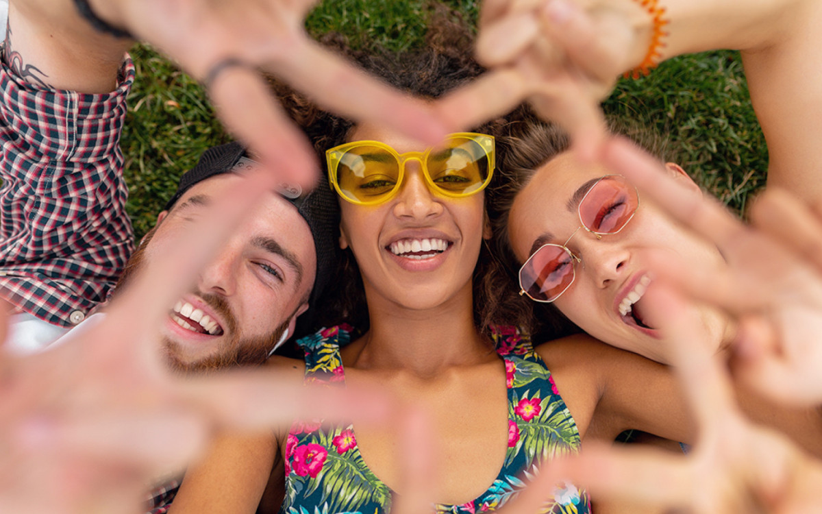 top view from above on colorful stylish happy young company of friends lying on grass in park, man and women having fun together, summer hipster fashion style, traveling smiling and showing peace sign