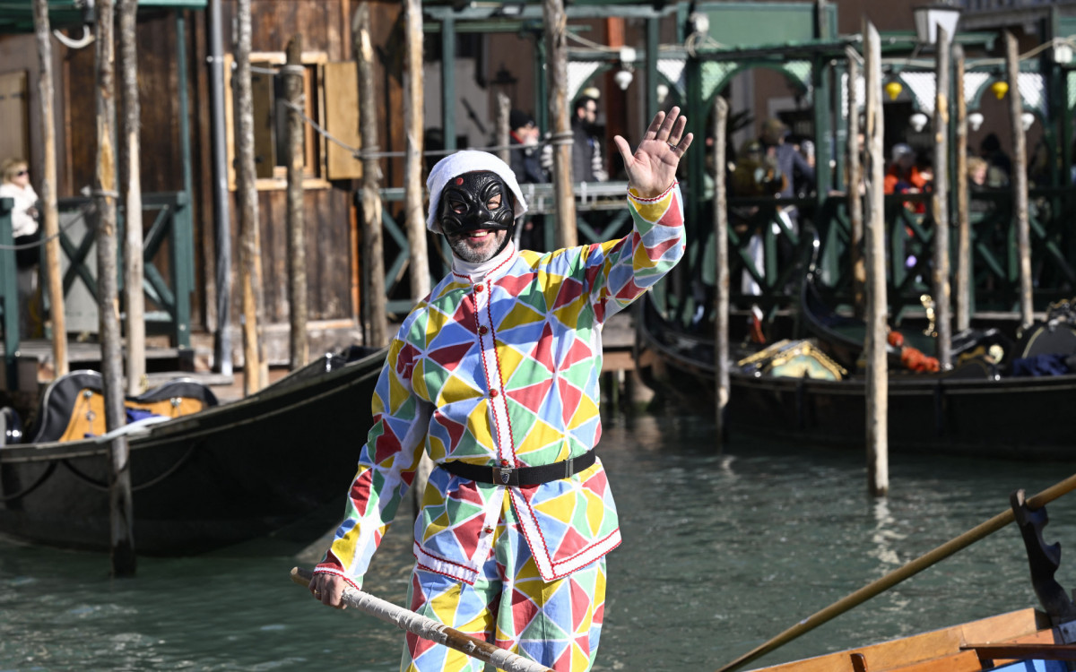 Homem vestido como Arlequim acena de seu barco durante um desfile no Grande Canal no Carnaval de Veneza
