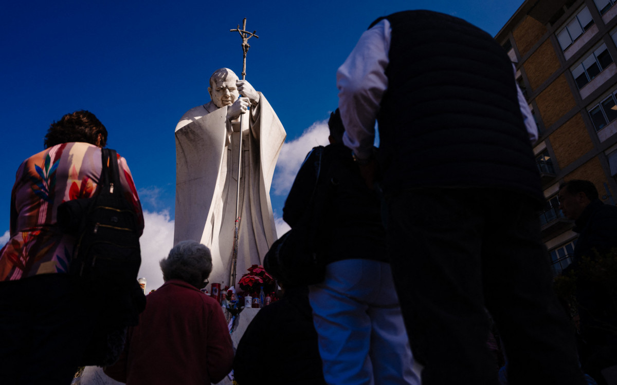 Em frente à estátua do falecido João Paulo II, fiéis rezam pelo Papa Francisco - AFP
