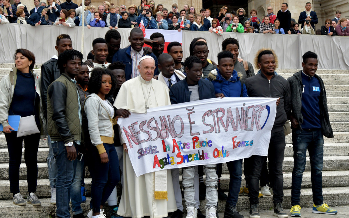 O papa Francisco posa com um grupo de migrantes na Praça São Pedro, no Vaticano. Na faixa, a mensagem: \'ninguém é estrangeiro\'