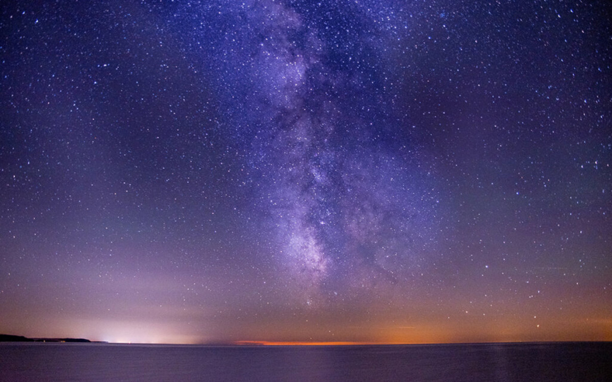 A breathtaking shot of the sea under a dark and purple sky filled with stars