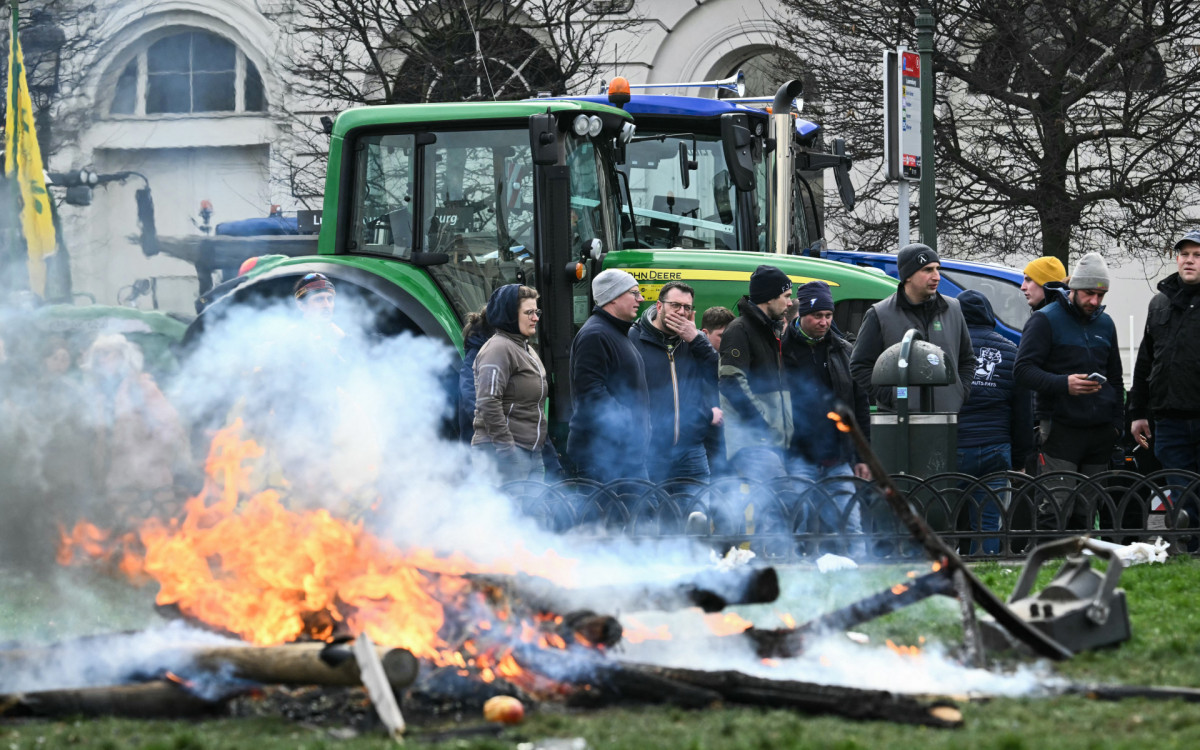 Agricultores se posicionam ao lado de tratores enquanto a fumaça sobe perto do Parlamento Europeu,  - AFP
