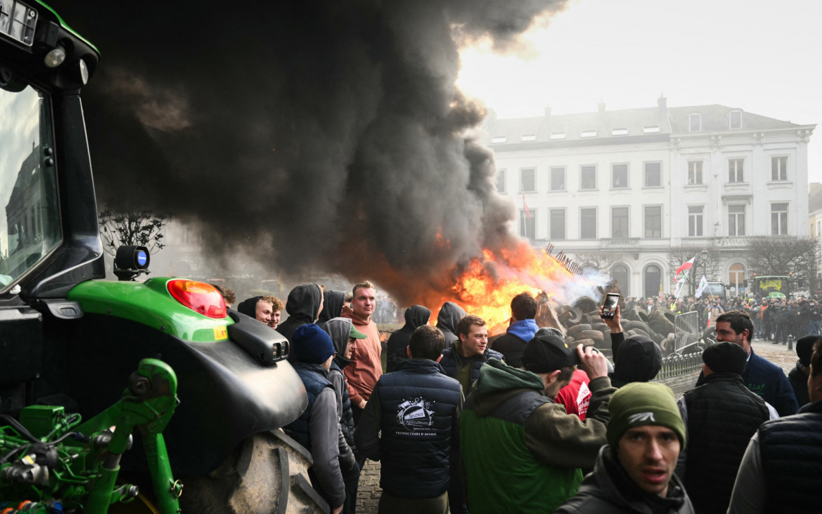 Agricultores se posicionam ao lado de tratores enquanto a fumaça sobe perto do Parlamento Europeu - AFP