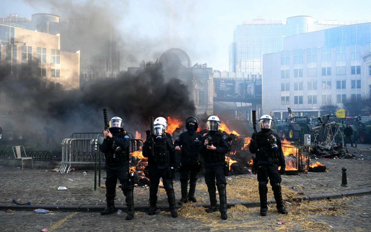 Agricultores se posicionam ao lado de tratores enquanto a fumaça sobe perto do Parlamento Europeu - AFP