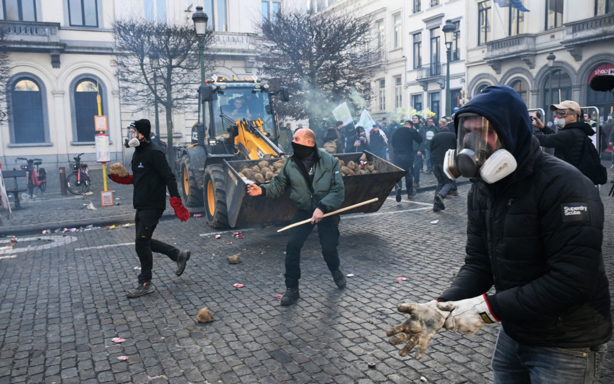 Agricultores se posicionam ao lado de tratores enquanto a fumaça sobe perto do Parlamento Europeu - AFP