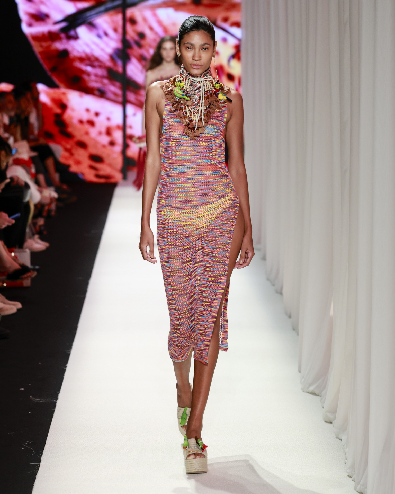 O tricô multicolorido com fenda lateral e acessórios de impacto traduz a vibração tropical da coleção com leitura contemporânea
