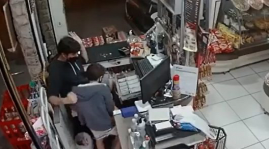 Uma criança que estava na padaria na hora do roubo é protegida pelo caixa da loja, no bairro Alphaville, em Campos - Reprodução de vídeo