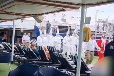 Funcionários de cruzeiro desfilam com trajes semelhantes aos da Ku Klux Klan